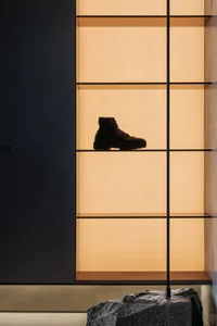 A minimalist retail space with glass walls displaying a single black boot on a shelf.