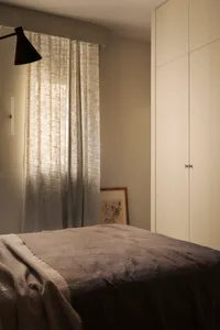 A minimalist bedroom with a bed covered in grey and blue textiles and wooden flooring.