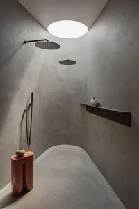 A minimalist bathroom with concrete walls, two overhead showers, and a small shelf with decorative items.