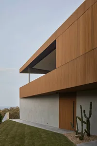 Modern residential building with wooden exterior panels and a patio overlooking greenery.