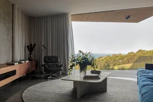 A modern living room featuring a concrete floor, minimalist furniture, and a view of the ocean through large windows.