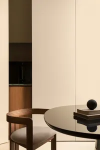 A modern, minimalist living room featuring a sleek glass dining table with a black tabletop and a single wooden chair with a