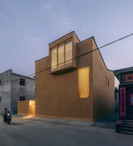 A modern building exterior made of wood, illuminated by warm lights from the interior.