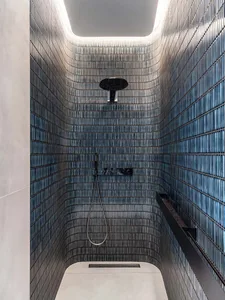 A minimalist bathroom with glass tiles, featuring a shower area with a ceiling light and a hand-held showerhead.