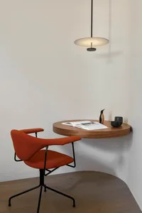 Modern home office setup with a round wooden table, orange chair, and pendant light.