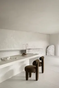 Minimalist kitchen with concrete countertops and floor, featuring a modern bar stool and minimalist furniture design.