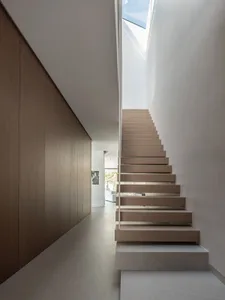 Modern minimalist wooden staircase with a sleek railing and natural light coming through a skylight.