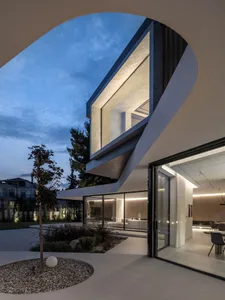 A modern house exterior at night with illuminated interiors and a landscaped garden.
