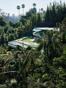 A modern house with glass and concrete exterior surrounded by trees.