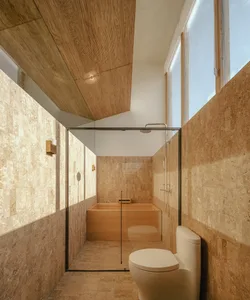 Modern bathroom featuring a marble bathtub and floor, glass shower enclosure, and toilet