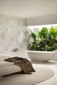 A modern minimalist bathroom with a concrete wall and a freestanding bathtub surrounded by lush green plants.