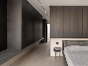 A modern minimalist bedroom featuring dark wood paneling and a light-colored hardwood floor.