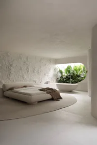 A minimalist bedroom featuring a concrete platform bed and bathtub in a circular room with greenery.