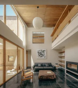 A modern minimalist living room with wooden accents, featuring a black leather sofa, wooden coffee table, and large windows w