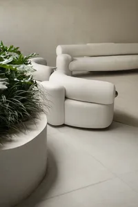 A modern white sofa with circular base and a matching white circular planter with green plants next to it.