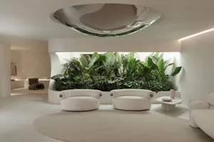 Modern interior design featuring white leather sofas and a circular coffee table with green plants in the background.