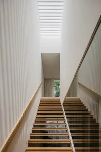 Modern minimalist staircase made of light-colored wood with a glass wall and a wooden handrail.
