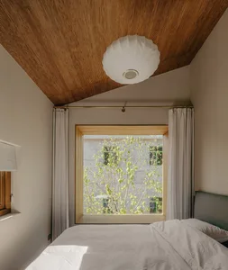Minimalist bedroom with white bed, large window, and green leaves outside
