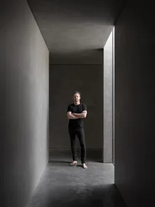 A minimalist interior with concrete walls and flooring in a narrow, well-lit corridor.