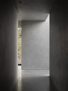 Minimalist interior with concrete walls, floors, and ceilings, leading to a natural light-filled space.