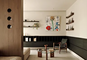 A minimalist living room with wood accents, glass coffee table, and metal-frame chair.