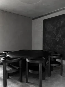 A minimalist black and wood restaurant dining room with a round table and chairs.