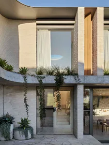 Modern architectural front featuring a concrete structure with large glass windows and greenery on the balcony.