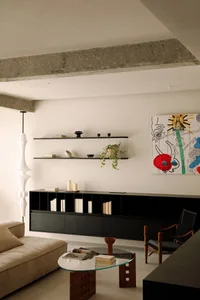 A modern living room with floating concrete shelves containing various decorative items and books, a beige sofa, a glass coff