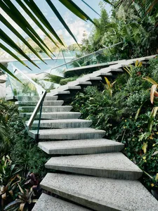 Concrete steps surrounded by lush greenery with a glass railing.
