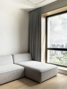 A minimalist living room featuring a grey sofa with a window overlooking a cityscape.