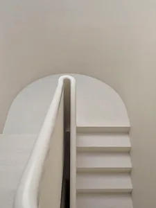 A minimalist concrete staircase with a white curved handrail.
