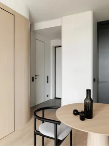 A sparse, minimalist entryway with light wood flooring, a white column, and black and gray accents.