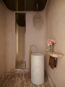 Modern bathroom with marble sink and floor, featuring a brass faucet and a chandelier with pink flowers on the shelf.