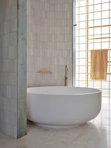 A modern bathroom featuring a freestanding bathtub, marble and brass accents, and tiled walls.
