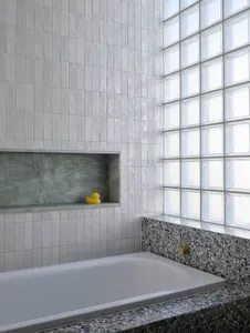 Modern bathroom interior featuring white terrazzo tiles, white bathtub, and a window with clear glass.