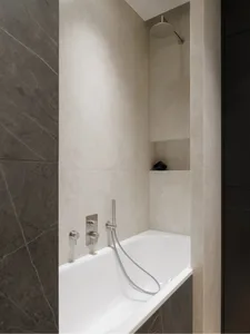 Modern bathroom featuring tiled walls and a sleek bathtub with a handheld showerhead.