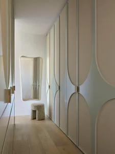 Modern closet with linen fabric wall covering, circular door designs, and a stool with a textured surface.