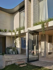 A modern exterior designed with concrete materials, featuring a curved roof, large windows, and climbing vines.