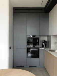 A modern minimalist kitchen with grey cabinets, an oven, and a coffee machine on a countertop.