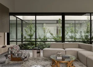 A modern minimalist living room with a large glass wall, neutral textiles, and greenery.