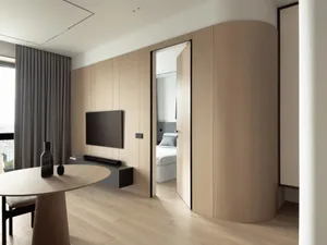 A modern minimalist living room with a round wooden table and curved wooden cabinet.