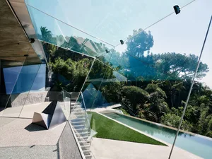Modern residential house featuring glass walls and concrete structure surrounded by lush greenery.