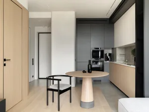 Modern, minimalist-style kitchen featuring sleek, gray cabinets and a round, wooden dining table with a black chair.