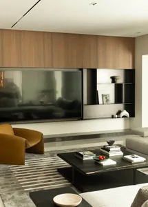 A modern, minimalist living room featuring a wooden wall unit, a leather armchair, a marble coffee table, and a large flat-sc