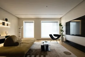 A modern living room with minimalist design, featuring neutral-toned furniture, large windows, and a black coffee table.