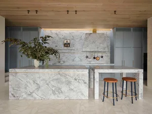 Modern residential kitchen featuring a large marble island with a vase of greenery and stools underneath.