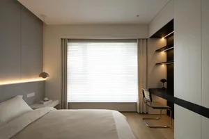 A minimalist bedroom featuring a taupe bed, a built-in desk, and neutral-toned curtains.