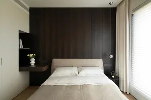 Modern minimalist bedroom featuring a wooden headboard and white bedding with a vase of flowers on a floating desk.