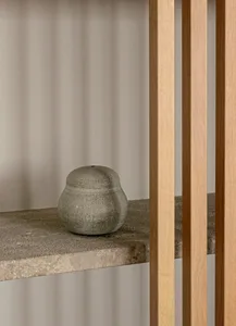 A minimalist concrete vase sits on a shelf.