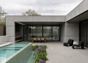 A modern, minimalist outdoor living area featuring a concrete swimming pool and deck with contemporary furniture.